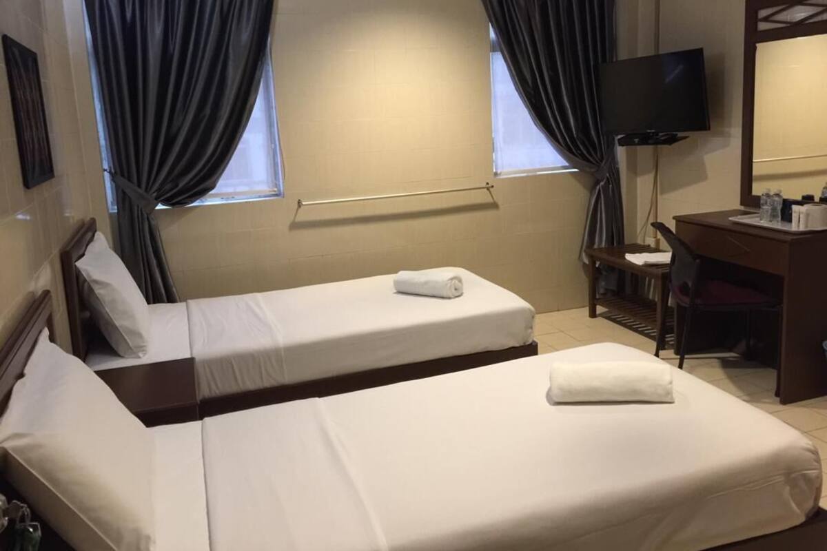 Hotellihuone, jossa on kaksi sänkyä, työpöytä, tuoli, televisio ja ikkuna, jossa on verhot.
