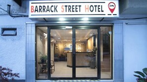 La entrada al Hotel Barrack Street, con mostrador de recepción, zona de estar y un cartel con el nombre del hotel.