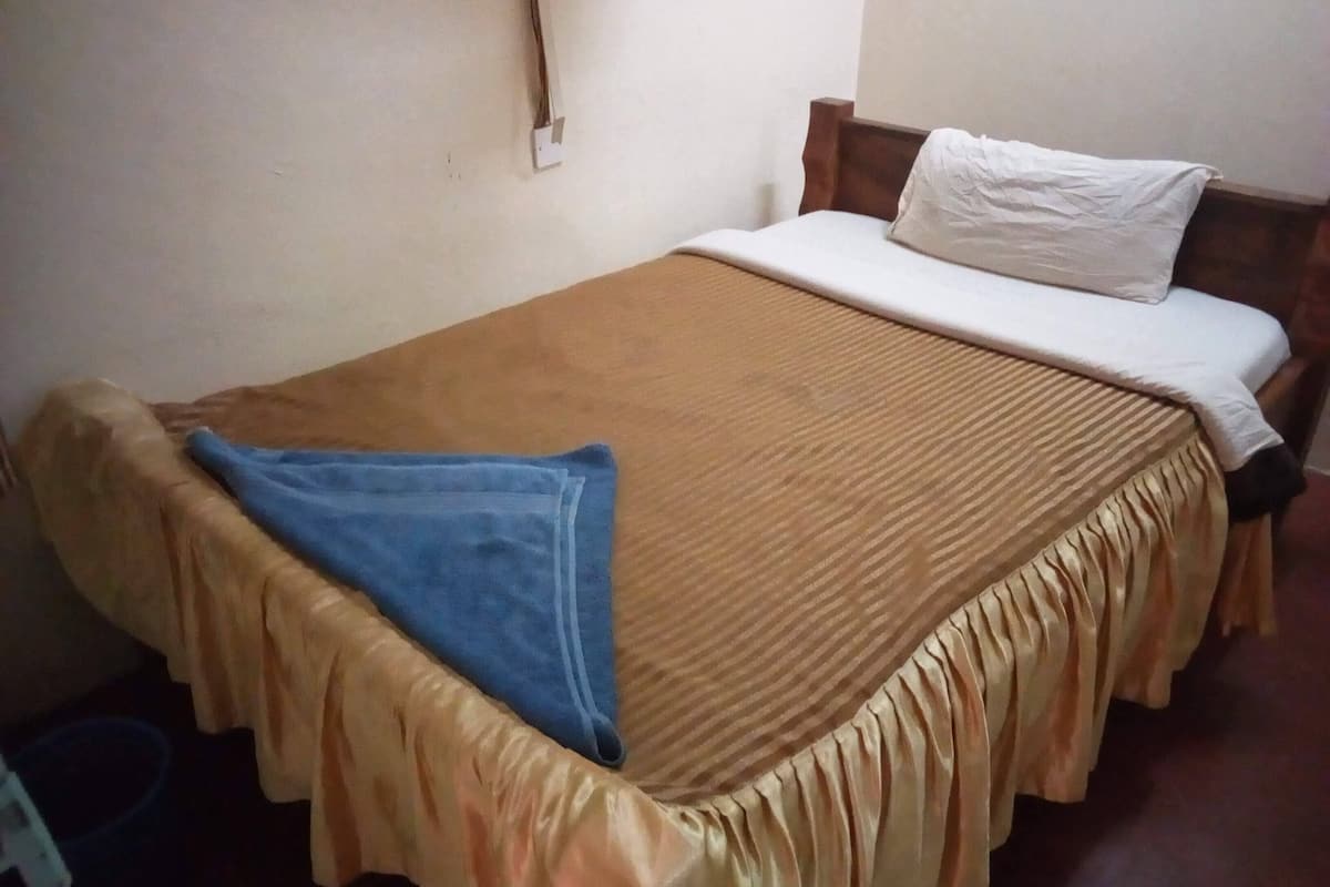 A single bed with a brown bedspread and a blue blanket, a white pillow, and a wooden headboard.