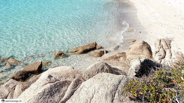A beach with clear turquoise water, white sand, and large rocks.