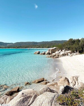 Una playa con agua turquesa cristalina, arena blanca y rocas grandes.