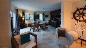 A spacious living area with a dining table, chairs, a sofa, and a decorative ship's wheel.