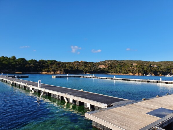 Un muelle se adentra en una masa de agua azul cristalina, con un paisaje montañoso al fondo.