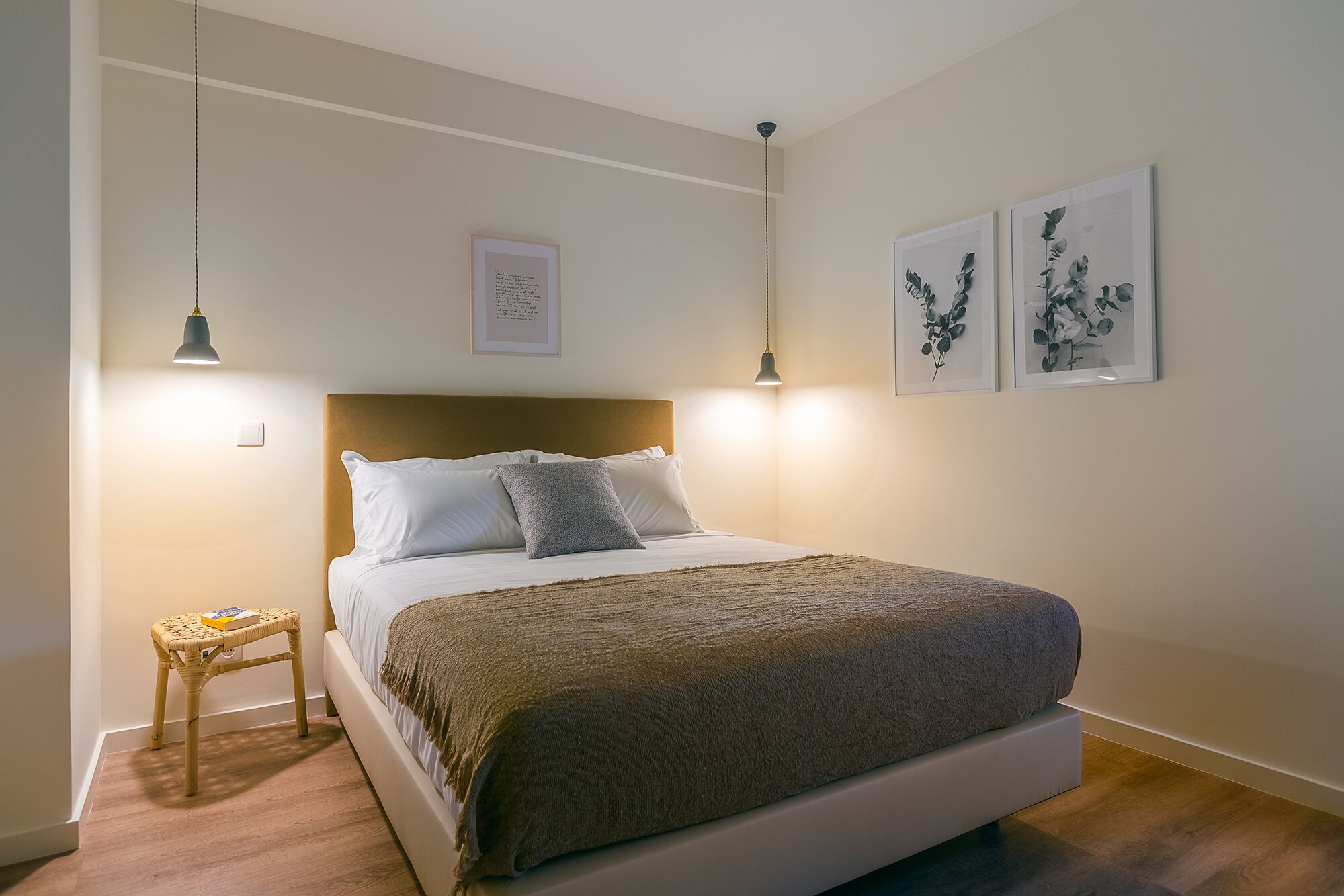 Une chambre à coucher bien rangée, avec un lit, une table de chevet et des œuvres d’art accrochées au mur.