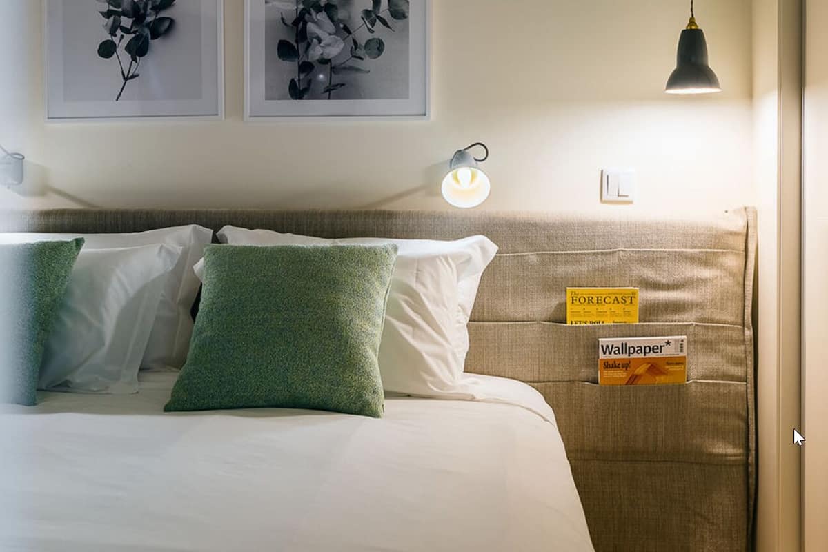 A neatly made bed with green pillows, a headboard with a sign, and a wall-mounted light fixture.