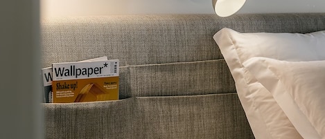 A hotel room with a bed, a wall-mounted lamp, a framed inspirational quote, and a magazine on the headboard.
