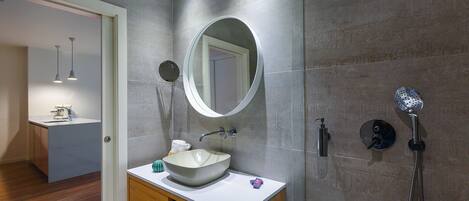 A modern bathroom with a large mirror, a vessel sink, a handheld showerhead, and a wall-mounted faucet.