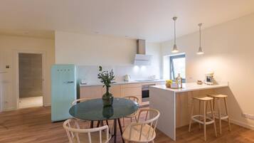 A modern kitchen with a dining area, featuring a central island with stools, a refrigerator, and pendant lighting.