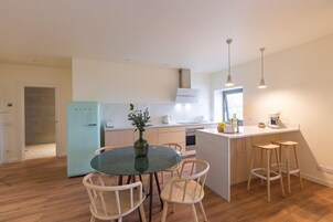 A modern kitchen with a dining area, featuring a central island with stools, a refrigerator, and pendant lighting.