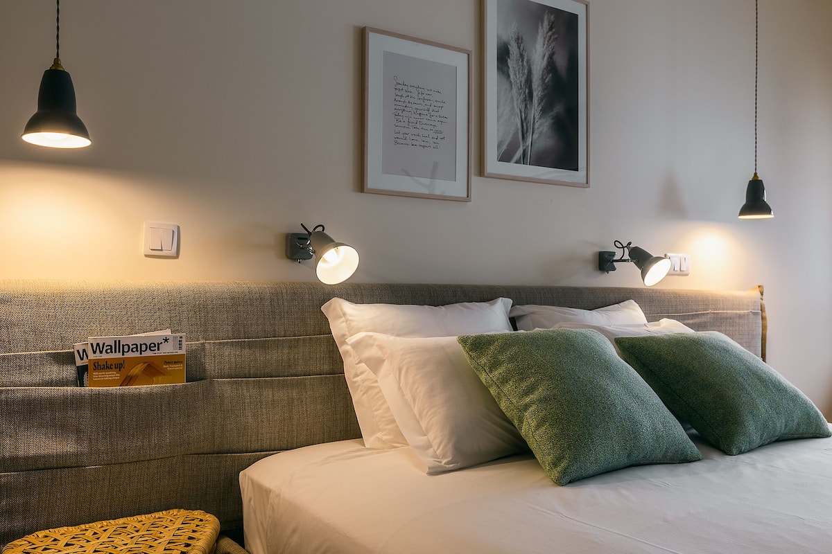 A neatly arranged hotel room with a large bed, two wall-mounted reading lamps, a framed quote on the wall, and a magazine on the side table.