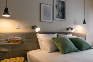Une chambre d’hôtel bien aménagée, avec un grand lit, deux lampes de lecture fixées au mur, une citation encadrée accrochée au mur et un magazine posé sur la table de chevet.