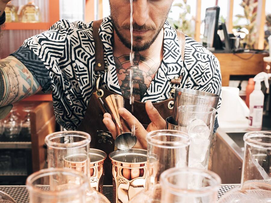 A person preparing drinks in a bar setting with multiple glasses and bottles.
