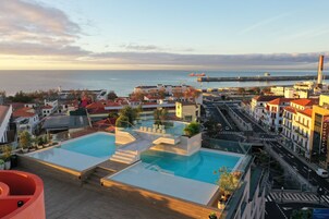 A rooftop pool with a view of the sea and cityscape.