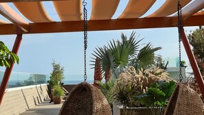 A wooden pergola with hanging rattan swings, potted plants, and a view of the ocean. - Three House Hotel (Funchal)