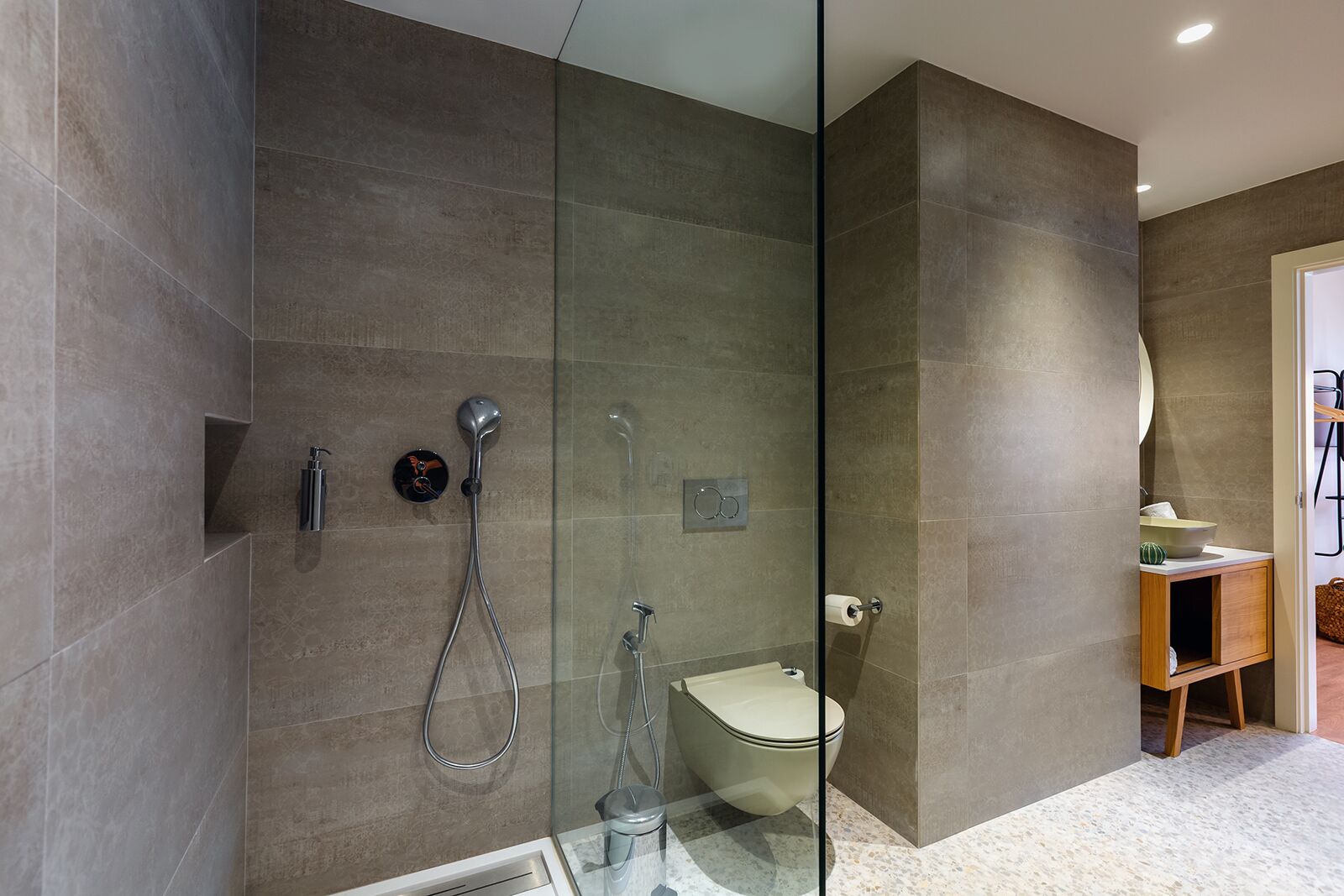 A modern bathroom with a glass-enclosed shower, a toilet, and a small wooden vanity with a bowl sink.