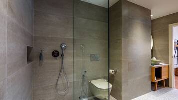 A modern bathroom with a glass-enclosed shower, a toilet, and a small wooden vanity with a bowl sink.