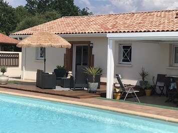Vue arrière de la villa avec petit salon sur terrasse en bois exotique.