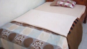 Ein Einzelbett mit Holz-Kopfteil, einer zudeckenden Bettwäsche mit Blumenmuster und einem Kissen mit Schachbrettmuster.
