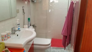 A bathroom with a sink, toilet, and shower. There are toiletries on the sink and a pink towel hanging on the shower door. - Casa Mari Playa De Mogan (Mogan)
