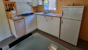 Et kompakt køkken med hvide skabe, en gasblus, en vask og et køleskab.