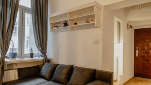 A modern living room with a sectional sofa, a window with curtains, and built-in shelves with decorative items. - Warsaw Concierge Loft Chmielna (Warsaw)