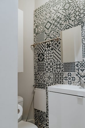 A bathroom with a patterned tile wall, a toilet, and a sink with a mirror.