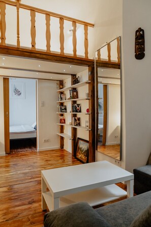 A room with a wooden floor, a white table, a bookshelf, and a bed with a white headboard.