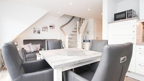 A modern kitchen with a dining area, white cabinets, a microwave, and a staircase. - Blinkfüür No.25 (Krummhoern)