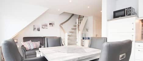 A modern kitchen with a dining area, white cabinets, a microwave, and a staircase.