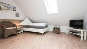 A modern, well-lit room with a bed, a television, a wicker chair, and a small plant. - Blinkfüür No.25 (Krummhoern)
