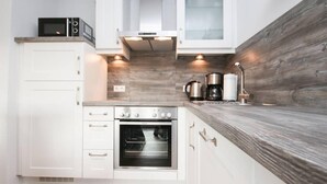 A compact kitchen with white cabinetry, a built-in oven, a microwave, and a wooden backsplash. - Blinkfüür No.25 (Krummhoern)