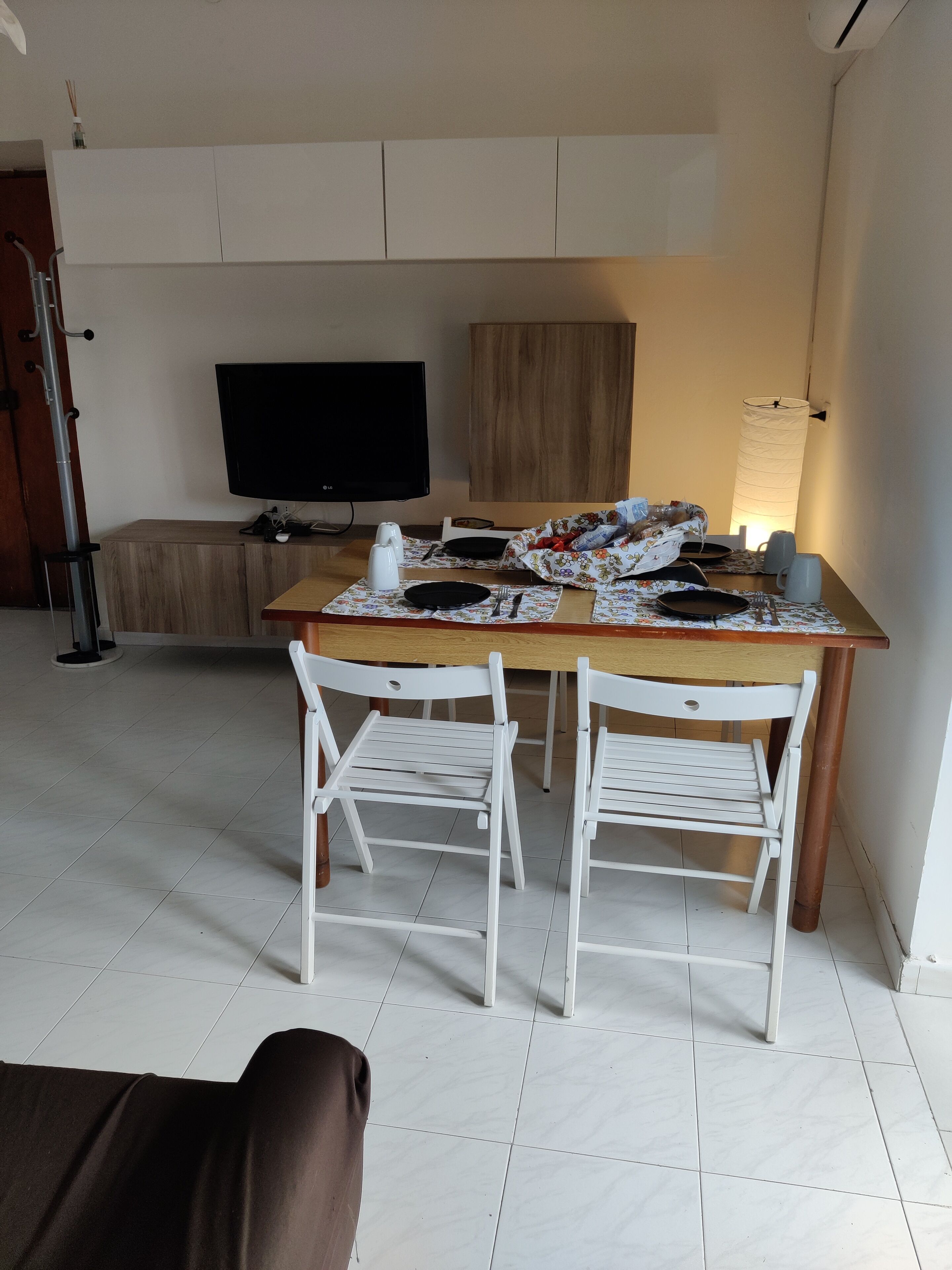 Ein Essbereich mit Holztisch, zwei weißen Stühlen, einem Fernseher und einer Lampe.