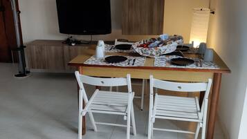 Ein Essbereich mit Holztisch, zwei weißen Stühlen, einem Fernseher und einer Lampe.