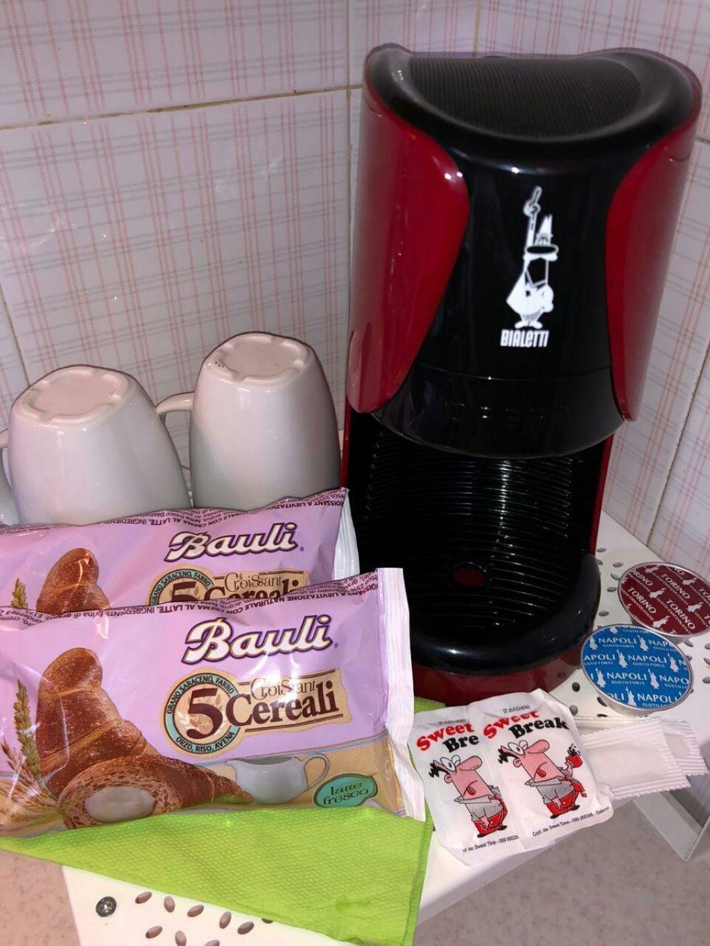 Uma cozinha com cafeteira, caixas de cereal e um saco de biscoitos.