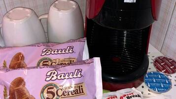 Uma cozinha com cafeteira, caixas de cereal e um saco de biscoitos.