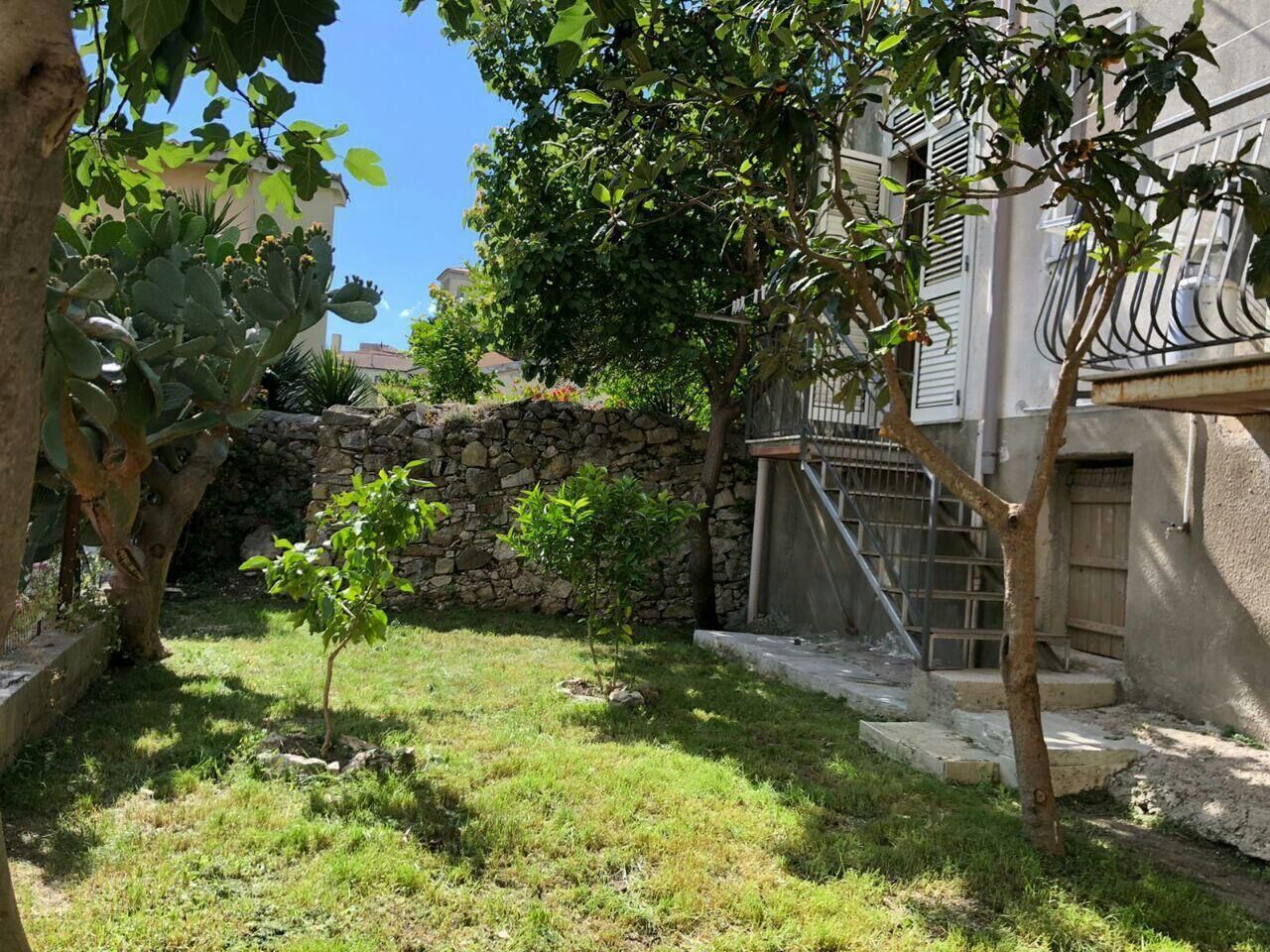 A small garden with a stone wall, a tree, and a building with a balcony.