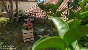 Eine Terrasse mit Tisch und Stühlen, eine Holzkiste mit Blumen und im Hintergrund ein Ziegeldach sowie Berge.