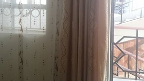 Una habitación con ventana que presenta celosías metálicas decorativas y una cortina de estampado ondulado.