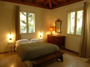 Ein Schlafzimmer mit einem Bett, Nachttischlampen, einem Schminktisch, einem Spiegel und Fenstern mit Vorhängen.