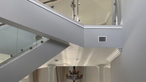 Ein geräumiger, moderner Innenraum mit einer Glasstufenwendel, einem Kristallleuchter und Blick durch große Türen nach draußen.