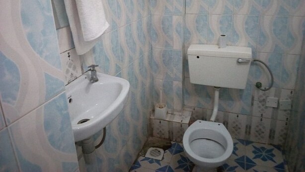 A small bathroom with a sink, toilet, and patterned tiles. - Royal Prince 2 Hotel (Meru)