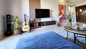 A modern living room with a flat-screen TV, a guitar, a blue sofa, a dining table, and a decorative vase. - Apartment Bagatelle (Marrakech)