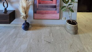 A modern lobby with a marble floor, a framed artwork of a staircase, a hanging light fixture, a vase with pampas grass, and a potted plant. - Apartment Bagatelle (Marrakech)