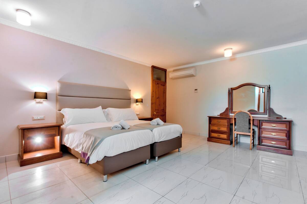 A modern bedroom with a large bed, bedside lamps, a wooden dresser, and a mirror.