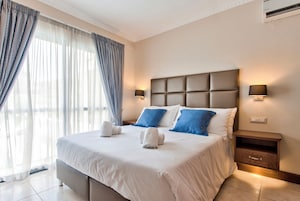 A neatly made bed with white and blue pillows, a headboard, and a nightstand with a lamp.