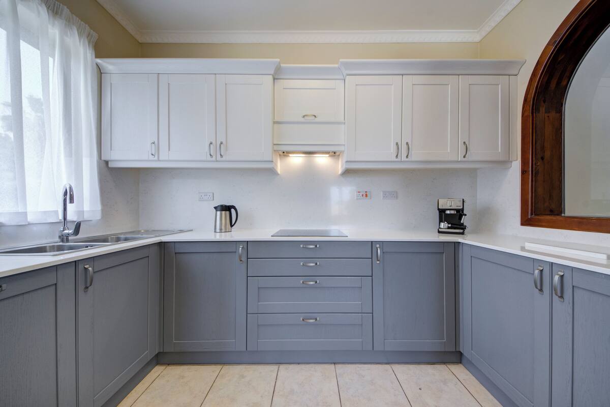 A kitchen with grey cabinets, a white countertop, a coffee maker, and a kettle.