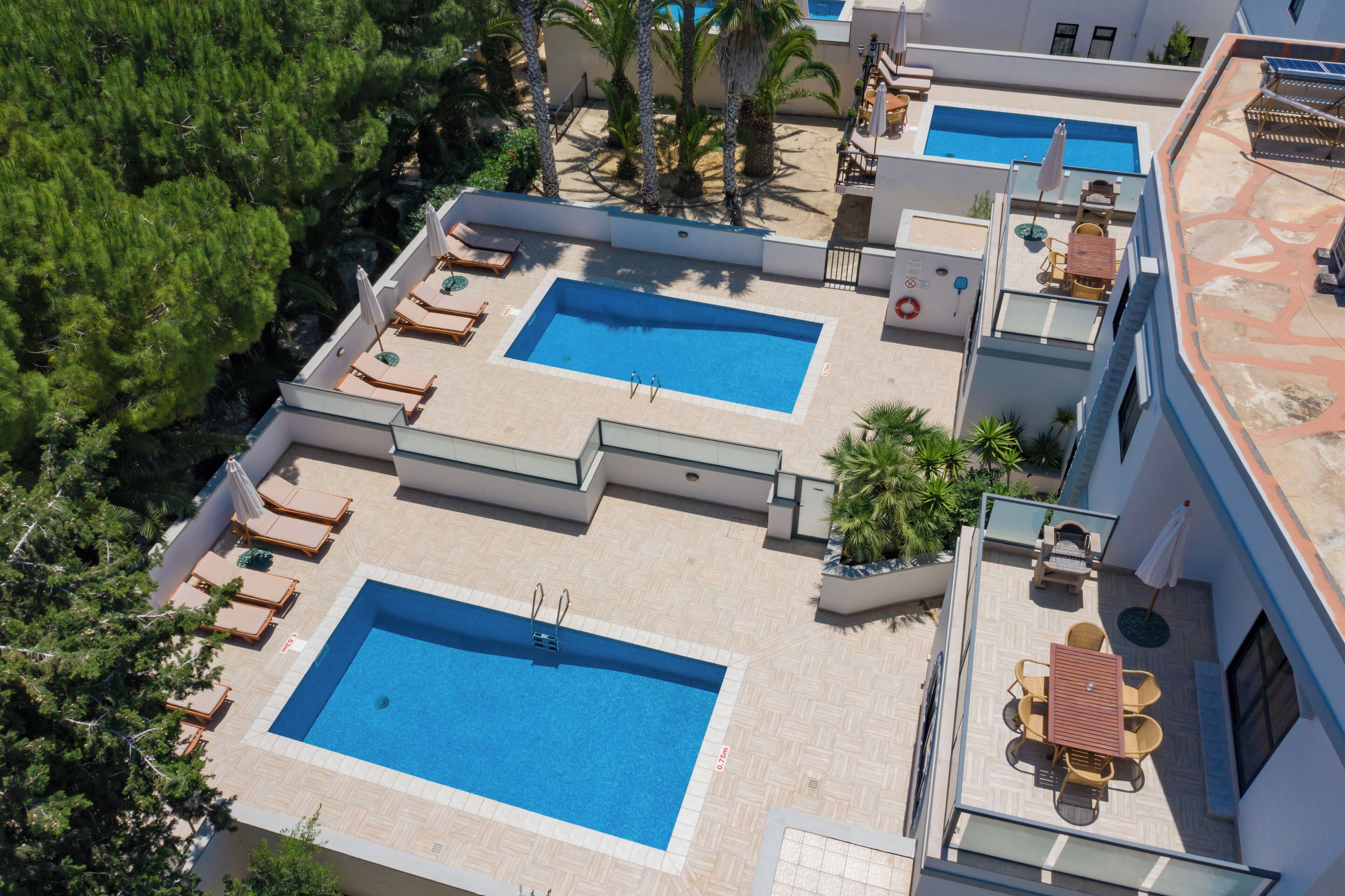 A rooftop pool area with multiple swimming pools, sun loungers, and a dining area with outdoor furniture.