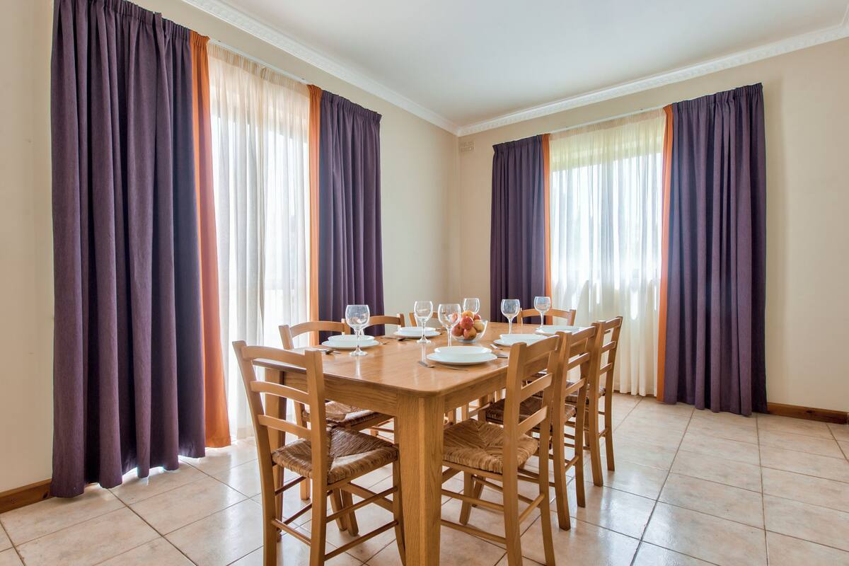 A dining room with a wooden table set for six, surrounded by chairs.