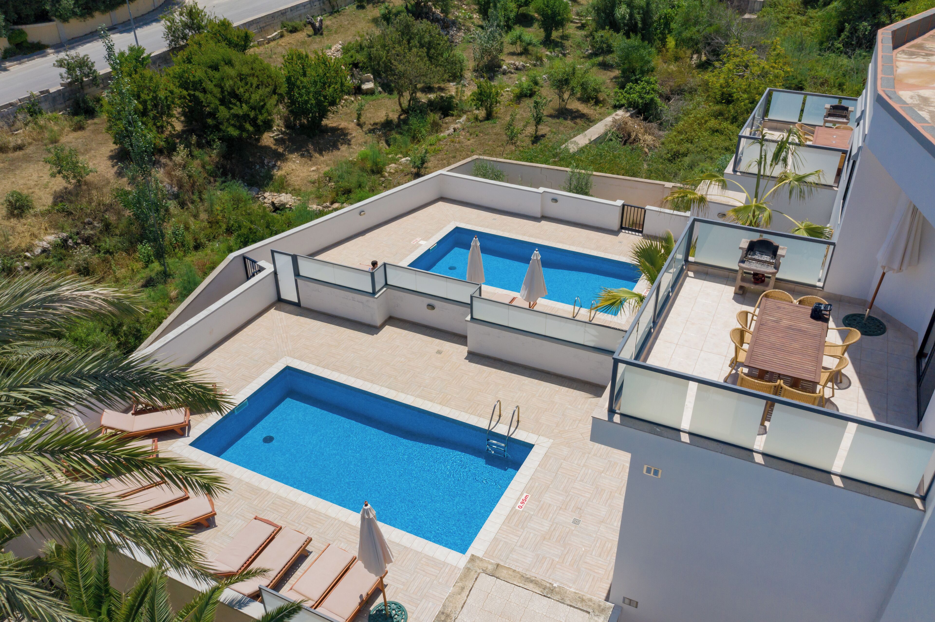A rooftop pool area with two pools, lounge chairs, and a table with umbrellas.