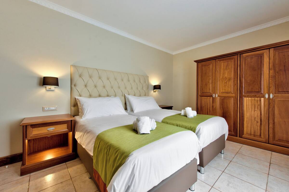 A hotel room with a large bed, two bedside tables, a wardrobe, and a wall-mounted lamp.